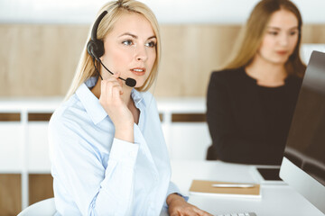 Blonde business woman sitting and communicated by headset in call center office. Concept of telesales business