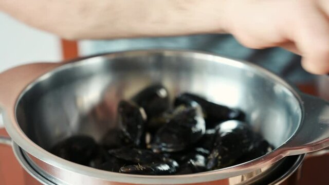 Close-up footage of the hands of a middle-aged Caucasian man who is cleaning mussels: one by one he tears the thread that keeps them attached. Preparation of a food of the Mediterranean diet.