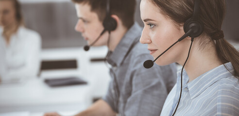 Call center. Group of casual dressed operators at work. Brunette business woman in headset at customer service office