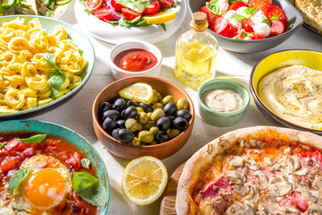 Set of different Mediterranean foods: olives, mozzarella and tomato salad, Greek salad, pasta, tortellini ravioli, pizza, pita lavash sandwich, shish kebab, shakshuka, hummus, top view