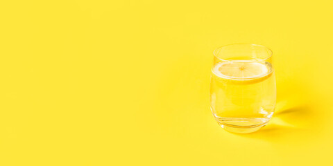 Glass of water with lemon on a yellow background. Summer refreshing drink.
