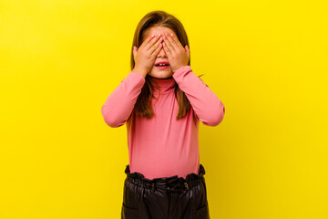 Little caucasian girl isolated on yellow background covers eyes with hands, smiles broadly waiting for a surprise.