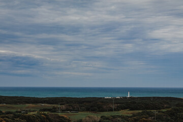 Fototapeta na wymiar Coastal view of lighthouse on the coast with green country farmland in the foreground