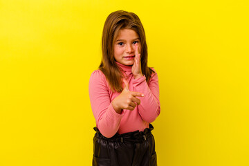 Little caucasian girl isolated on yellow background saying a gossip, pointing to side reporting something.