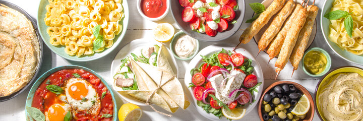 Set of different Mediterranean foods: olives, mozzarella and tomato salad, Greek salad, pasta, tortellini ravioli, pizza, pita lavash sandwich, shish kebab, shakshuka, hummus, top view