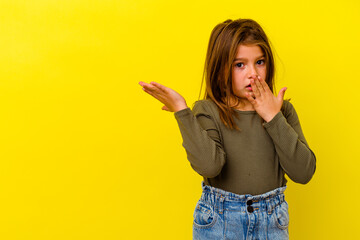 Little caucasian girl isolated on yellow background impressed holding copy space on palm.