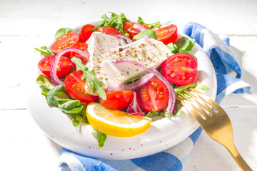 Mediterranean traditional food. Greek style salad, with fresh cherry tomatoes, lettuce, feta cheese, onions. Top view on white wood background