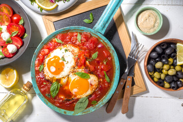 Traditional greek food, Shakshouka. eggs poached in frying pan with tomatoes, olive oil, peppers, onion, garlic, Mediterranean cuisine. Keto, fodmap low carb diet recipe, white wooden background