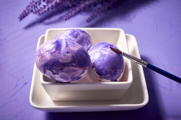 Coloring eggs with a brush. Easter tradition. Painted eggs on a purple watercolor background and purple lavender flowers.