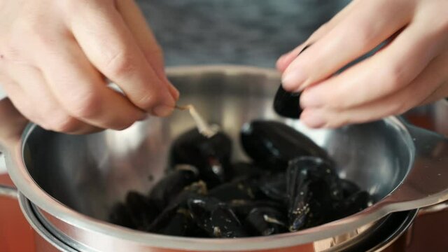 Close-up footage of the hands of a middle-aged Caucasian man who is cleaning mussels: one by one he tears the thread that keeps them attached. Preparation of a food of the Mediterranean diet.