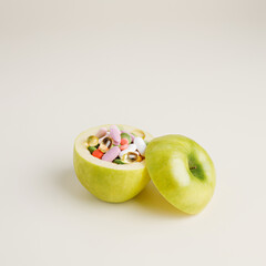 Fresh ripe green apple full of colorful vitamin pills and tablets on bright beige background. Creative healthy diet concept.