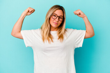 Young mixed race woman isolated on blue background showing strength gesture with arms, symbol of feminine power