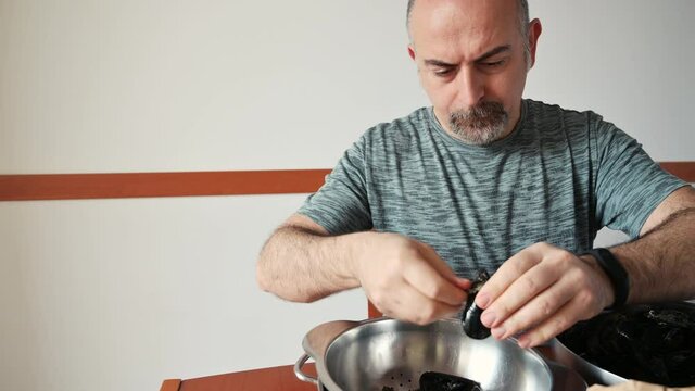 A middle-aged Caucasian man is cleaning some mussels: one by one he tears the thread that holds them attached. Preparation of a food of the Mediterranean diet.