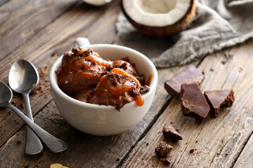 Chocolate coconut vegan ice cream in a white cup. Ice cream balls with chocolate and caramel. Wooden background, copy space.