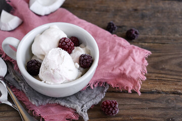 Coconut vegan ice cream in a white cup. Sundae balls. Ice cream with berries and raspberries. Wooden background, copy space.