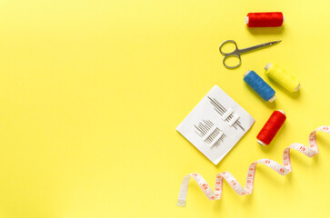 Flat lay of sewing accessories. Threads, needles, centimeter and scissors on yellow background, space for text