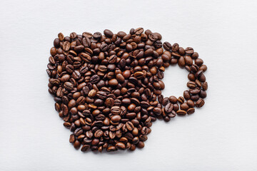 Coffee cup made of dark roasted coffee beans on white aquarelle paper background.  Horizontal format