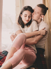 Couple at home dressed in home clothes sitting on the windowsill