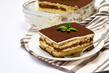 Traditional Italian Tiramisu dessert in glass baking dish, portion on plate and scapula isolated on white background