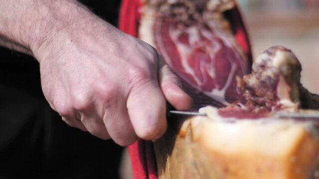 Male cutting a slice of dried spanish jamon serrano on wood table.