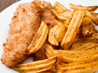 Traditional fish and chips dish on white plate. Common take away meal in English speaking nations. Cooked cod with peppered potato fries. Close up