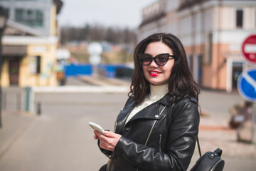 Obraz premium A beautiful hipster girl with a phone in her hands walks down the street