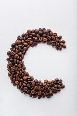 C character made of dark roasted coffee beans on white aquarelle paper background
