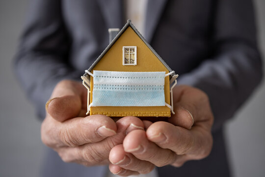 Senior businessman holding model house wearing protective medical mask in hands