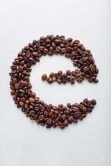 E character made of dark roasted coffee beans on white aquarelle paper background