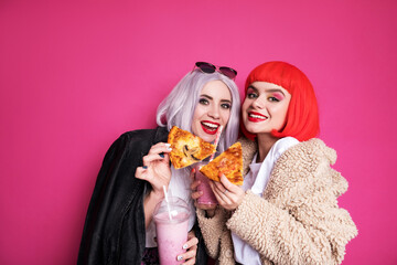 Two cute girl friends woman looking like teenagers standing on a pink background. They wearing...