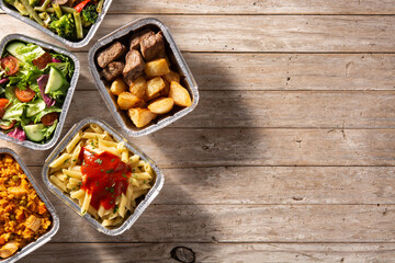 Take away healthy food in foil boxes on wooden table. Top view. Copy space	