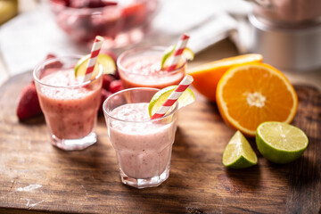 Various fruit smoothies in glass cups with paper straws and wedges of lime and more citruses on the side