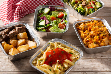 Take away healthy food in foil boxes on wooden table. 