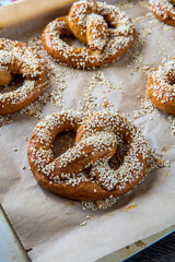 Selective focus on a freshly baked homemade soft pretzel with sesame seeds and garlic flakes, ready to eat. Tasty gluten free savory pastry with a knot placed in a baking tray, hot from the oven.
