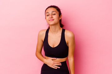 Young sport Indian woman isolated on pink background touches tummy, smiles gently, eating and satisfaction concept.