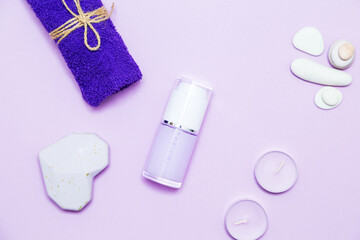Scented candles, towel, lotion and pebbles on a lilac background.