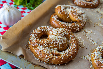 Freshly baked homemade soft pretzels with sesame seeds and garlic flakes, ready to eat. Tasty gluten free savory pastry with a knot on a vibrant, colorful, background. Coriander and garlic knob aside.