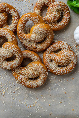 Freshly baked homemade soft pretzels with sesame seeds and garlic flakes, ready to eat. Tasty gluten free savory pastry with a knot on a brown background. Coriander and garlic knob aside. Copy Space