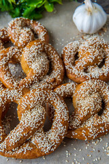 Pile of freshly baked homemade soft pretzels with sesame seeds and garlic flakes, ready to eat. Tasty gluten free savory pastry with a knot on baking sheet. Coriander and garlic knob in background.