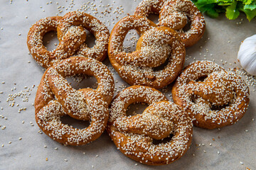 Freshly baked homemade soft pretzels with sesame seeds and garlic flakes, ready to eat. Tasty gluten free savory pastry with a knot on baking sheet. Coriander and garlic knob in background. Side view