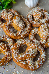 Freshly baked homemade soft pretzels with sesame seeds and garlic flakes, ready to eat. Tasty gluten free savory pastry with a knot on baking sheet. Coriander and garlic knob in background. Side view
