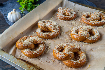 Freshly baked homemade soft pretzels with sesame seeds and garlic flakes, ready to eat. Tasty gluten free savory pastry with a knot placed in a baking tray. Coriander and garlic knob in the background