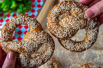 Hands holding two freshly baked homemade soft pretzels with sesame seeds and garlic flakes, ready to eat. Tasty gluten free savory pastry with a knot on a vibrant, colorful background. Selective focus