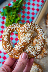 Hand holding freshly baked homemade soft pretzel with sesame seeds and garlic flakes, ready to eat. Tasty gluten free savory pastry with a knot on a vibrant, colorful background. Selective focus.