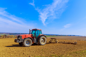 Fototapeta premium A farmer plows the soil in the field with a chisel plow on a tractor. Agricultural tractor with a plow on farmland.