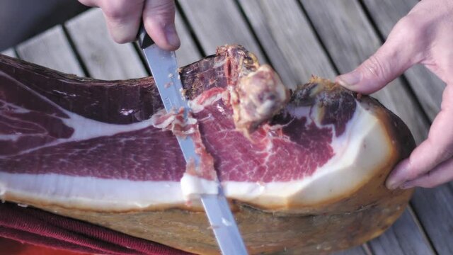 High angle view of man hand cutting a slice of dried spanish jamon serrano on wood table.