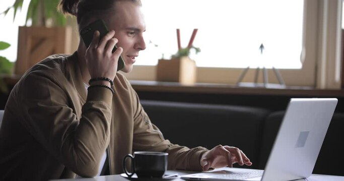 Young businessman working by laptop PC in a cafe and talking by phone