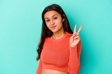 Young Indian woman isolated on blue background joyful and carefree showing a peace symbol with fingers.