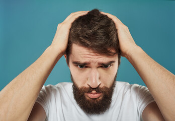 A man on a blue background is touching his head with his hands