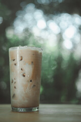 A glass coffee mix with milk on wooden table against nature background